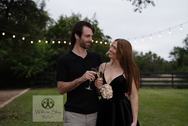 Engaged couple toasting champagne under string lights at Willow Sky Ranch near Fredericksburg TX