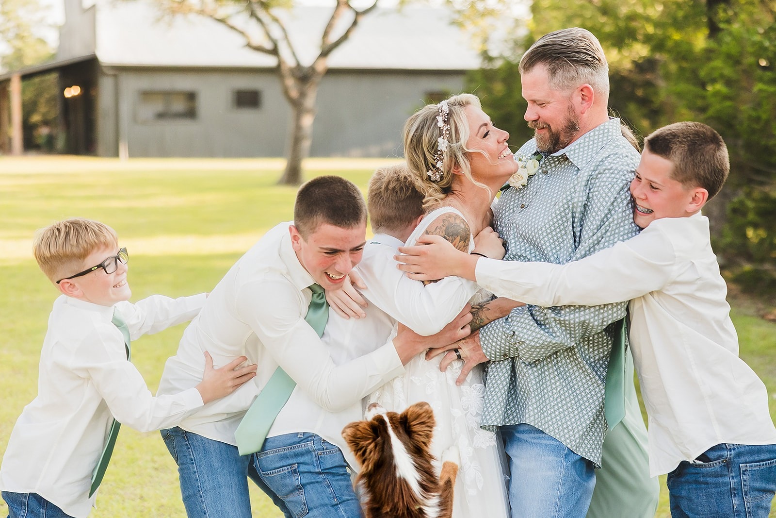Bride and groom surrounded by their boys in a joyful group hug on the lawn at Willow Sky Ranch — a blended family wedding celebration on the ranch grounds near Fredericksburg, Texas Hill Country