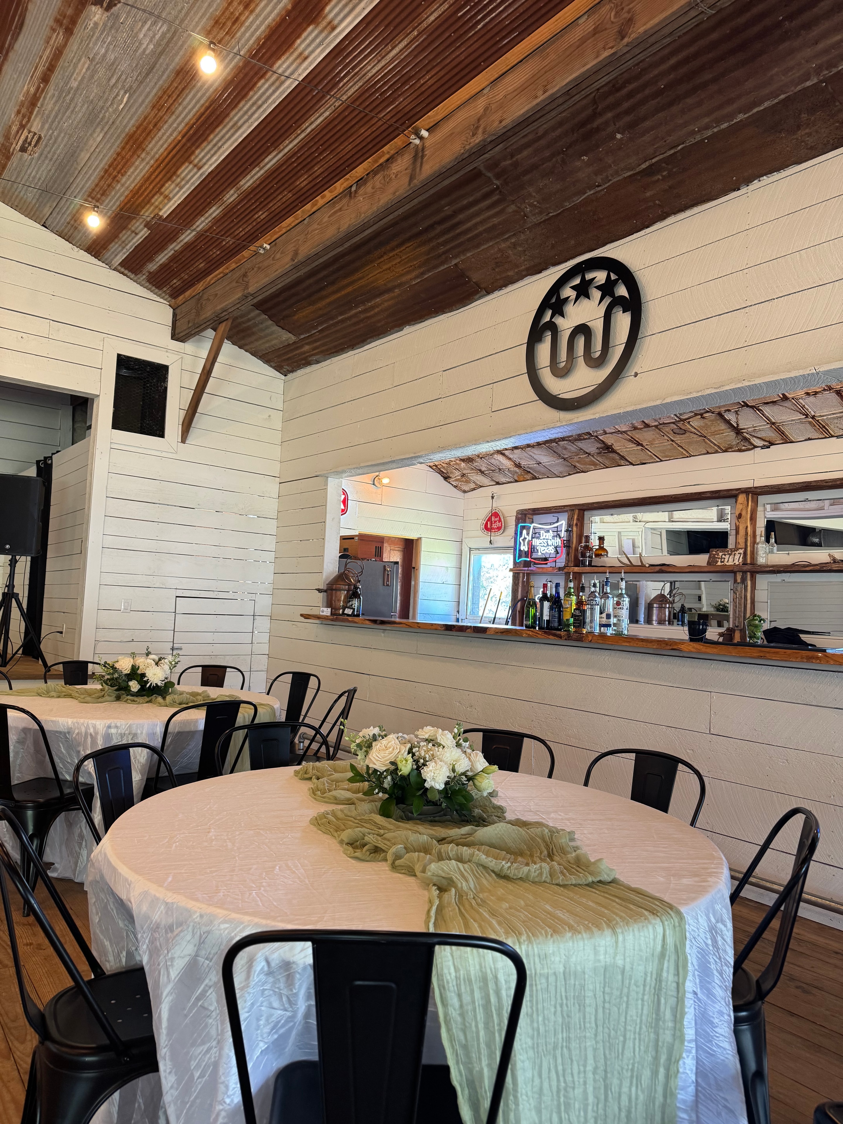Inside Willow Hall at Willow Sky Ranch — white shiplap walls, reclaimed wood accents, WSR metal monogram, and elegantly set reception tables with white floral centerpieces near Fredericksburg, Texas Hill Country