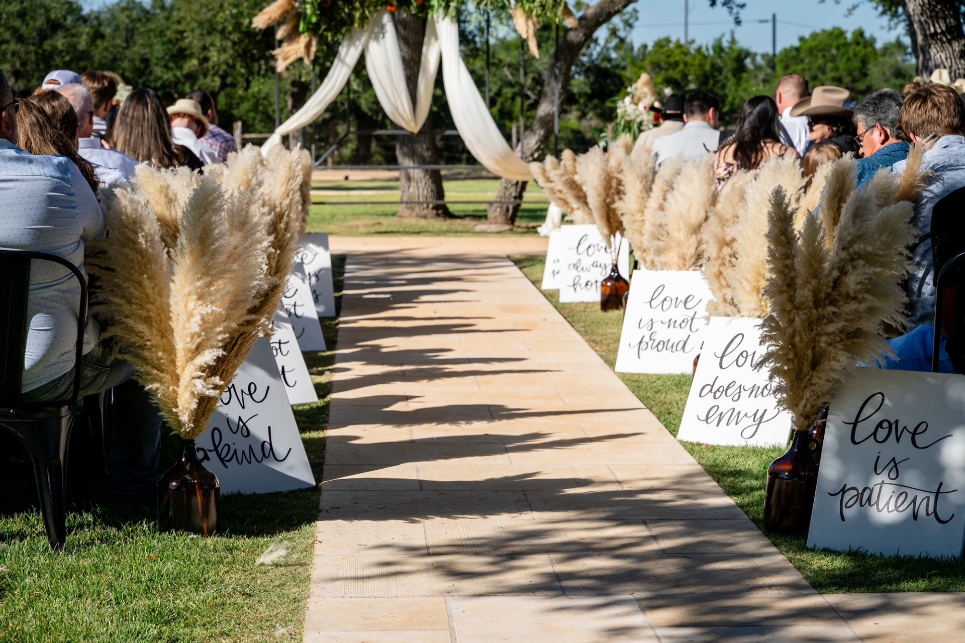 Fall wedding ceremony aisle at Willow Sky Ranch — pampas grass aisle markers with handwritten love scripture signs, outdoor ceremony under live oaks near Fredericksburg, TX