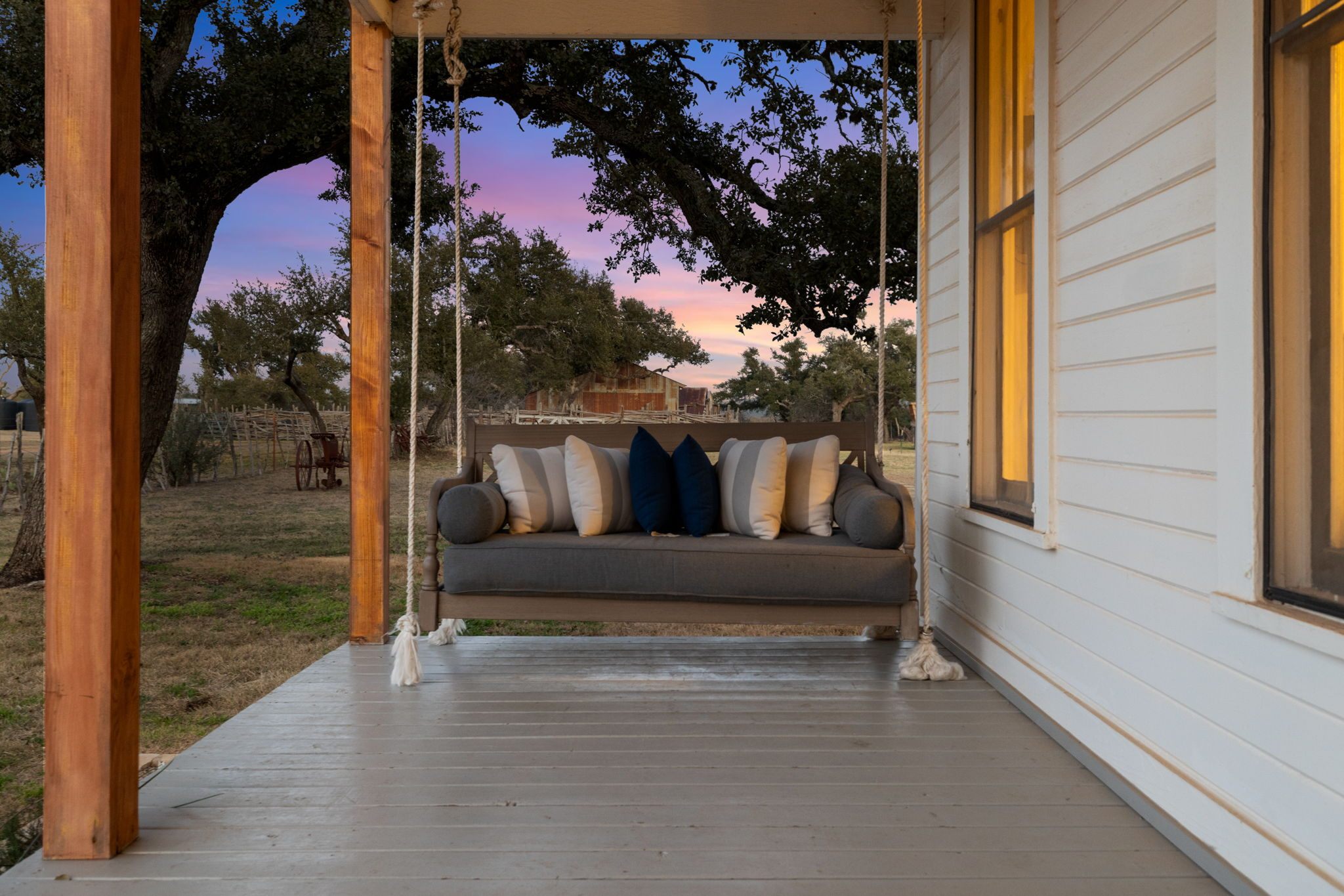 Bridal party on the covered front porch swing of The Greathouse at Willow Sky Ranch near Fredericksburg, TX — bridesmaids in champagne gowns laughing together on the historic 1905 farmhouse porch, Hill Country wedding venue near Austin and San Antonio, photographed by Madelyn Frost Photography
