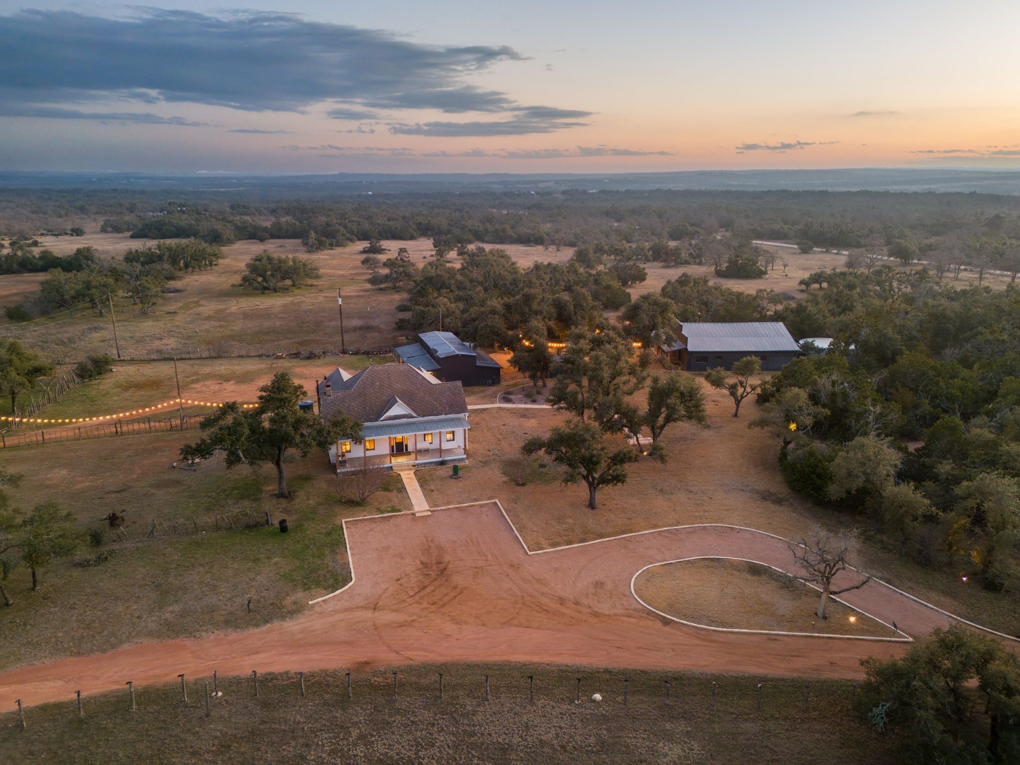 Aerial drone view of the entrance to Willow Sky Ranch near Fredericksburg, TX — Texas-shaped driveway, The Greathouse, Willow Hall, and sweeping Hill Country landscape at dusk, wedding venue near Austin and San Antonio