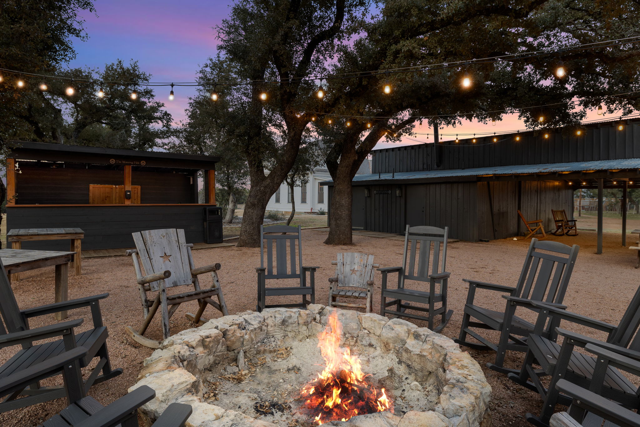 Stone fire pit with rocking chairs and bistro lights at Willow Sky Ranch at sunset